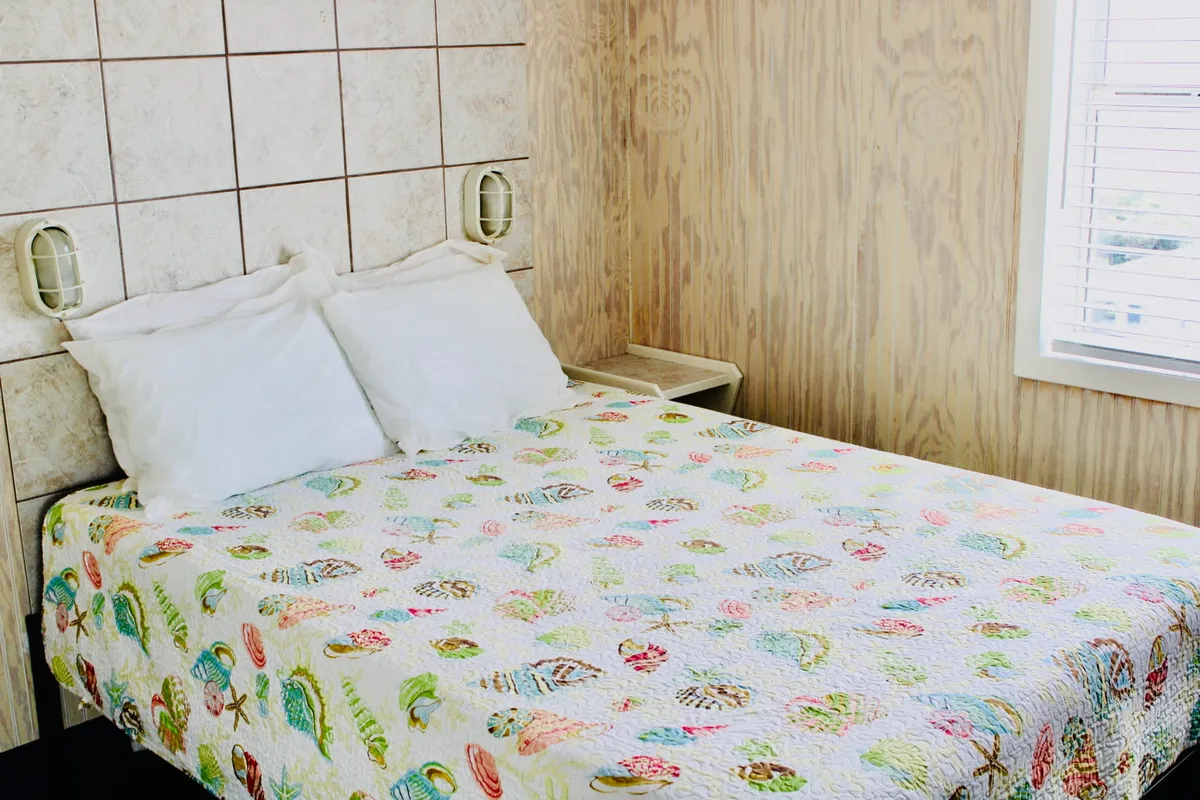 A cozy sleeping area with a bed adorned in a colorful quilt, warm wood paneling, and soft bedside lighting. Natural light fills the space, creating an inviting atmosphere perfect for unwinding and recharging.
